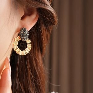 Macro view of gold wavy hoop earrings with navy blue pavé crystals on a model