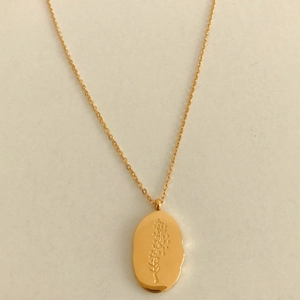 Detailed close-up of golden oval pendant with floral engraving on a fine link chain
