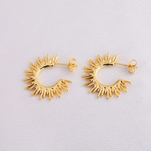 Detailed view of golden sunburst earrings with open hoop design on white textured fabric