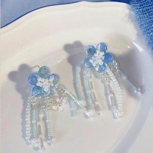Detailed view of handmade blue flower beaded earrings with tassels on a white ceramic plate