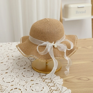 Detail of hand-woven straw hat with scalloped brim and white pearl chiffon bow ribbon