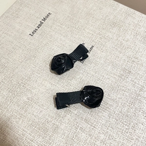 Detail view of two black satin ribbon rose flower hair clips with metal alligator base