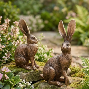 Pareja de estatuas de conejo de bronce realistas sobre piedras con musgo en jardín