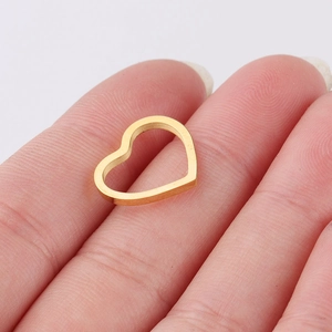 Close-up of a small golden hollow heart-shaped metal pendant held on a fingertip