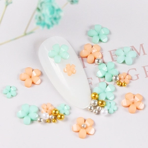 Detail of green and orange resin flower nail charms with gold beads on a white nail tip