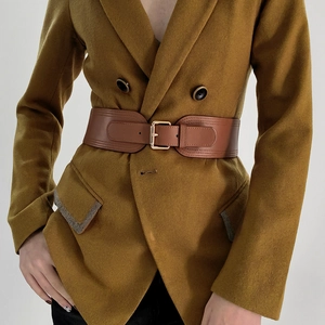 Brown wide elastic corset belt with golden pin buckle over a mustard yellow blazer