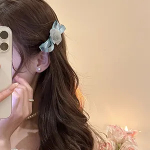 Elegant blue satin bow hair clip with white rose flower detail worn by a model