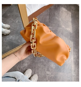 Detail of ginger orange pleated cloud pouch with thick gold metal chain strap handle