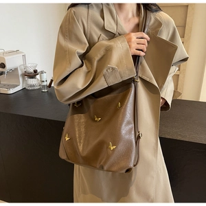 Detail of large brown PU leather shoulder bag with gold metal butterfly accents in a cafe