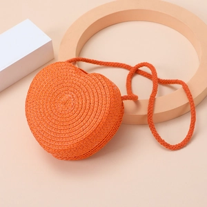 Detail of orange heart-shaped woven straw bag with rope strap on peach background