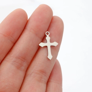 Miniature polished stainless steel silver cross pendant held by hand for size scale