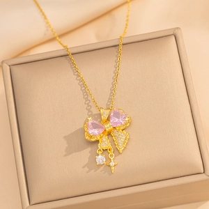 Golden bow necklace with pink heart gemstone and star charm on beige jewelry box