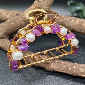 Detailed close-up of golden metal hair claw clip with amethyst stones and white pearls