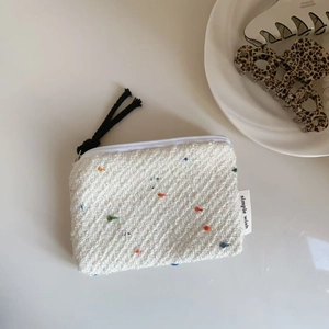 Dettaglio di mini pochette in tweed a pois colorati con tirazip nero su piatto