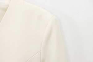 Detailed close-up of premium white blazer fabric texture and precision shoulder stitching