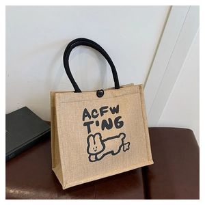 Close-up of beige linen tote bag with black woven handles and a cute rabbit print