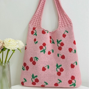 Pink knitted tote bag with red cherry patterns and green leaves on a clean background