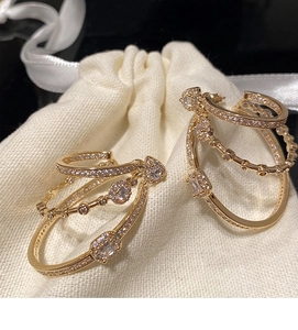 Detail of gold multi-layered zircon earrings placed on a beige fabric pouch with ribbon