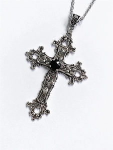 Close-up of vintage silver cross necklace with floral pattern and central black gem