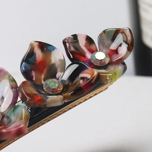 Macro detail of acetate flower hair clips with rainbow rhinestones and golden metal base