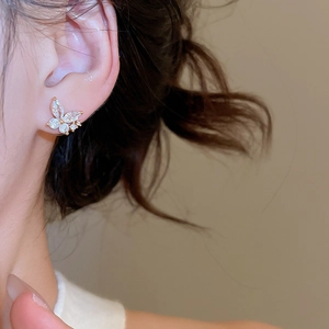 Detailed view of a gold-plated butterfly stud earring with cubic zirconia on a model's ear