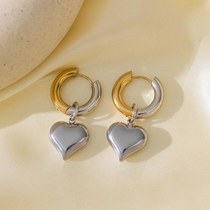 Detail of two-tone gold and silver heart pendant earrings on soft silk fabric