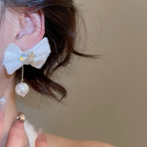 Close-up of white fabric bow earrings with pearl drop and star detail on model ear