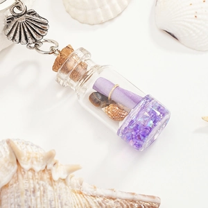Detailed close-up of a glass driftwood bottle keychain with purple sand and tiny seashells