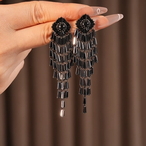 Detail of long black rhombus zircon tassel earrings held by hand for luxury styling