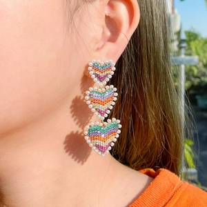 Boucles d'oreilles cœur arc-en-ciel avec strass et perles portées par un mannequin