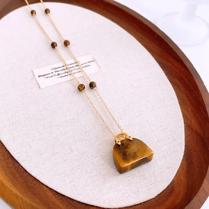 Dettaglio del ciondolo borsa in occhio di tigre su collana d'oro in vassoio legno