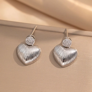 Silver textured heart drop earrings with round cubic zirconia on beige silk background