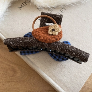 Detail view of tweed bow hair claw clip with crochet hat and flower on a book