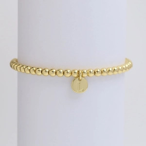 Macro detail of golden bead bracelet with letter L pendant on a white jewelry stand