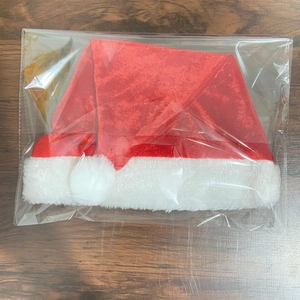Close-up of a red velvet Christmas hat with white plush trim in transparent packaging