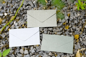 Detailed texture of mini linen paper envelopes in light grey and pea green on gravel