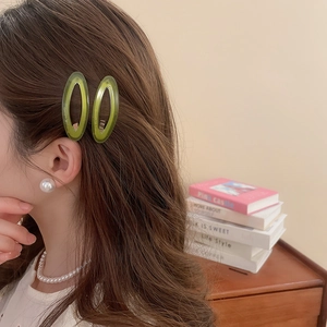Detail showing two translucent green acetate oval hair clips on a female model