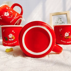 Three red ceramic Santa Christmas mugs with Merry Christmas lettering on a woven background