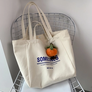 Detail of off-white canvas tote bag with blue text and a cute orange plush pendant