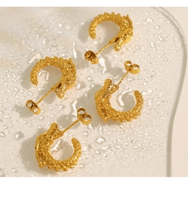 Macro shot of golden dragon-shaped C-earrings with detailed scales on water drops background