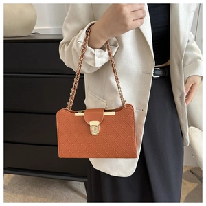 Detail of orange woven leather shoulder bag with gold chain strap on a model