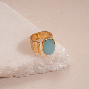Detail of a gold adjustable ring with an oval blue resin stone on a stone surface