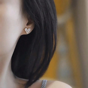 Close-up of minimalist silver heart stud earrings with cubic zirconia on model ear
