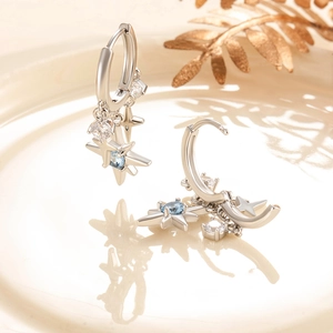 Silver star drop earrings with blue zircon stones on a decorative tray background