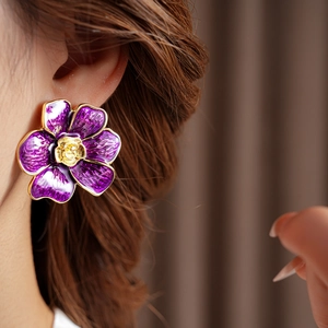 Primer plano de una modelo luciendo pendientes de flores en esmalte púrpura y dorado