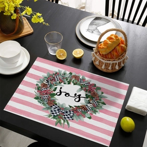 Close-up of pink striped Christmas placemat with Joy wreath on dark wood dining table