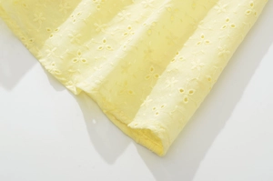 Dettaglio del ricamo sangallo giallo su un abito estivo con spalline sottili