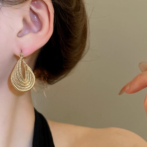 Detailed view of wide golden multi-layered textured metallic drop hoop earring on a model