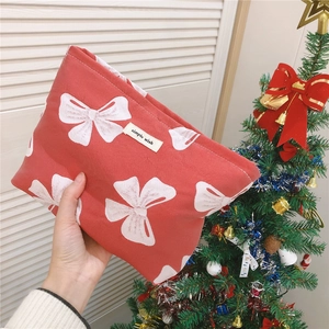 Detailed macro view of red canvas festive pouch featuring white bow patterns and logo patch