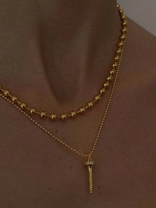 Layered gold nail pendant and beaded chain necklace shown on model's neck